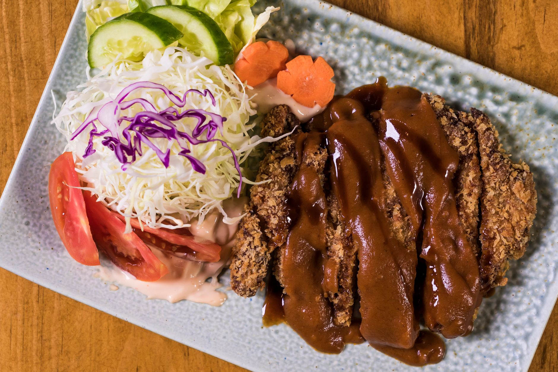 Potongan ayam katsu renyah, dilapisi tepung panggang keemasan, disajikan dengan saus tonkatsu dan irisan lemon